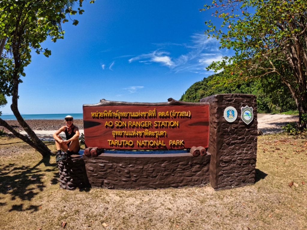 Woman sitting next to Tarutao National Park sign. 