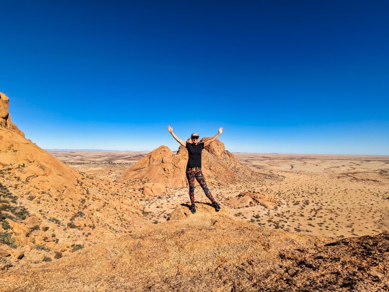 Dotti on top of a rock with a view of the Spitzkoppe plains below while enjoying some informal hiking