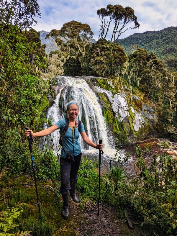 Dotti standing next to a waterfall on the Rwenzori Mountains Kilembe Trail